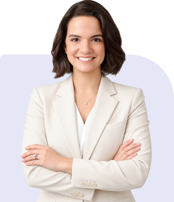 Woman with short brown hair wearing a cream-colored blazer stands with arms crossed, smiling at the camera against a light background.